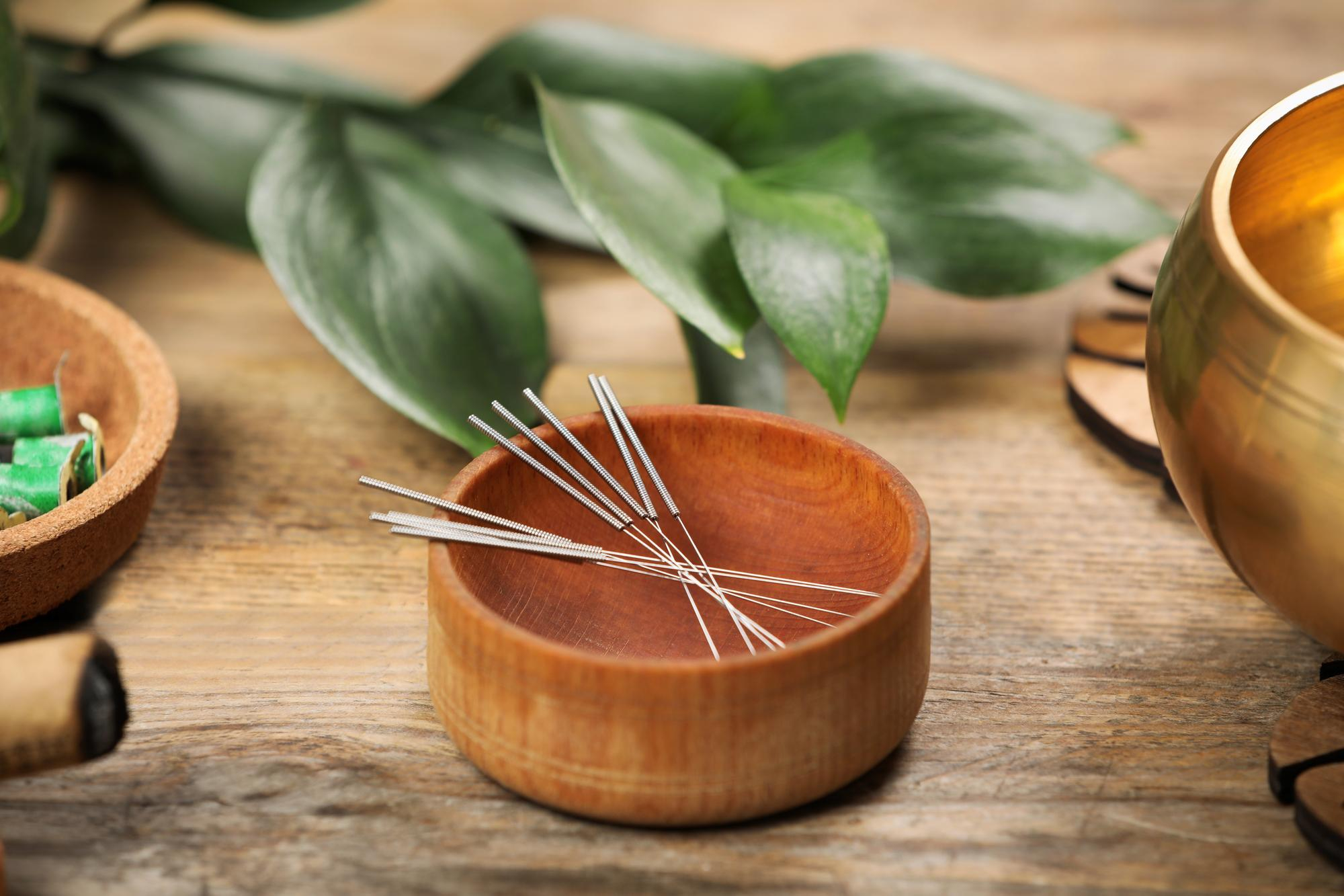 acupuncture needles in wooden bowl next to natural remedies